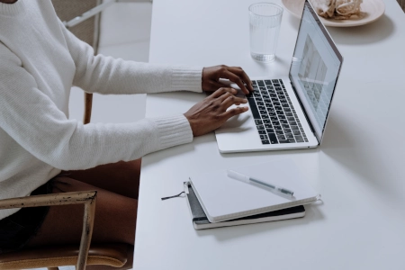 Hände tippen auf Laptop-Tastatur Notizblock daneben